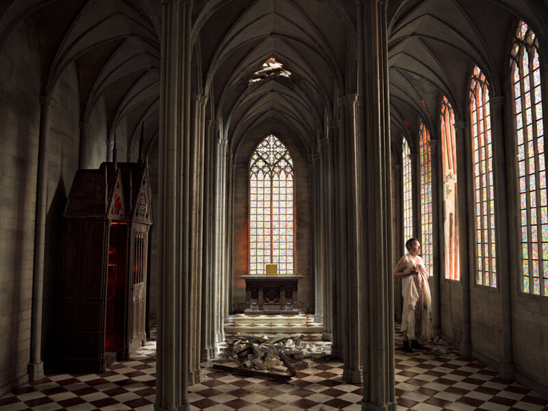 Man dressed in white robes looking out stain glassed cathedral window 