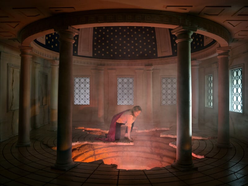 woman in red kneeled over glowing rupture in the ground, surrounded by columns 