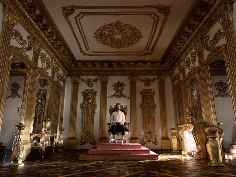 man wearing a white shirt sitting on throne in a  large room 