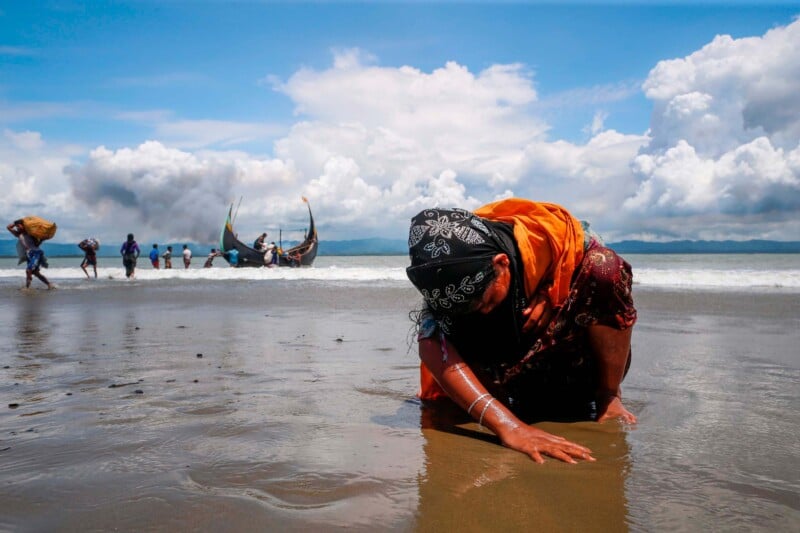 An exhausted Rohingya refugee woman touches the shore after crossing the Bangladesh-Myanmar border