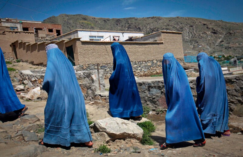 Afghan women clad in burqa walk up a hill