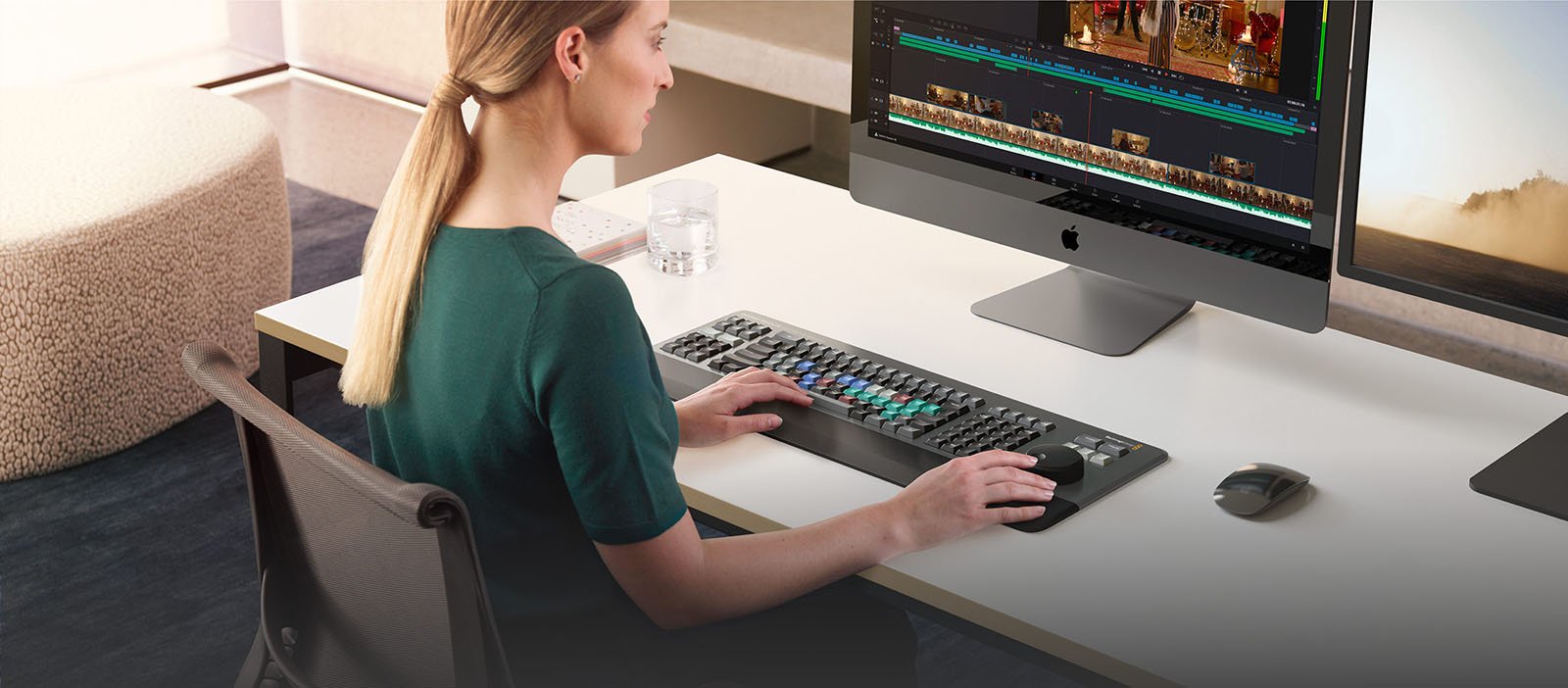 A woman sits at a desk using the DaVinci Resolve Editor keyboard with a computer.