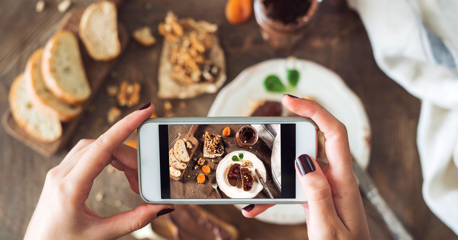 Hands holding a phone are seen taking a picture of food.