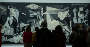 A crowd of people is seen viewing Pablo Picasso's Guernica.