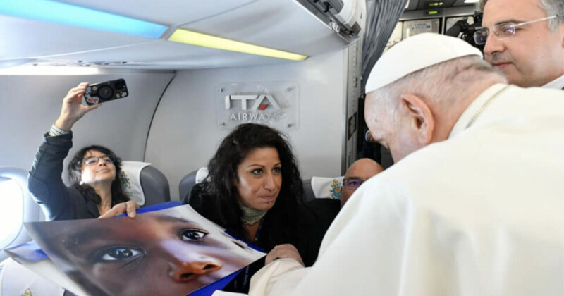 Pope Francis is shown a photo of a migrant child. 