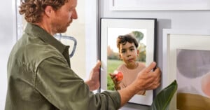A man hangs up a photo of a child on the wall using the Aura Frames Walden model.