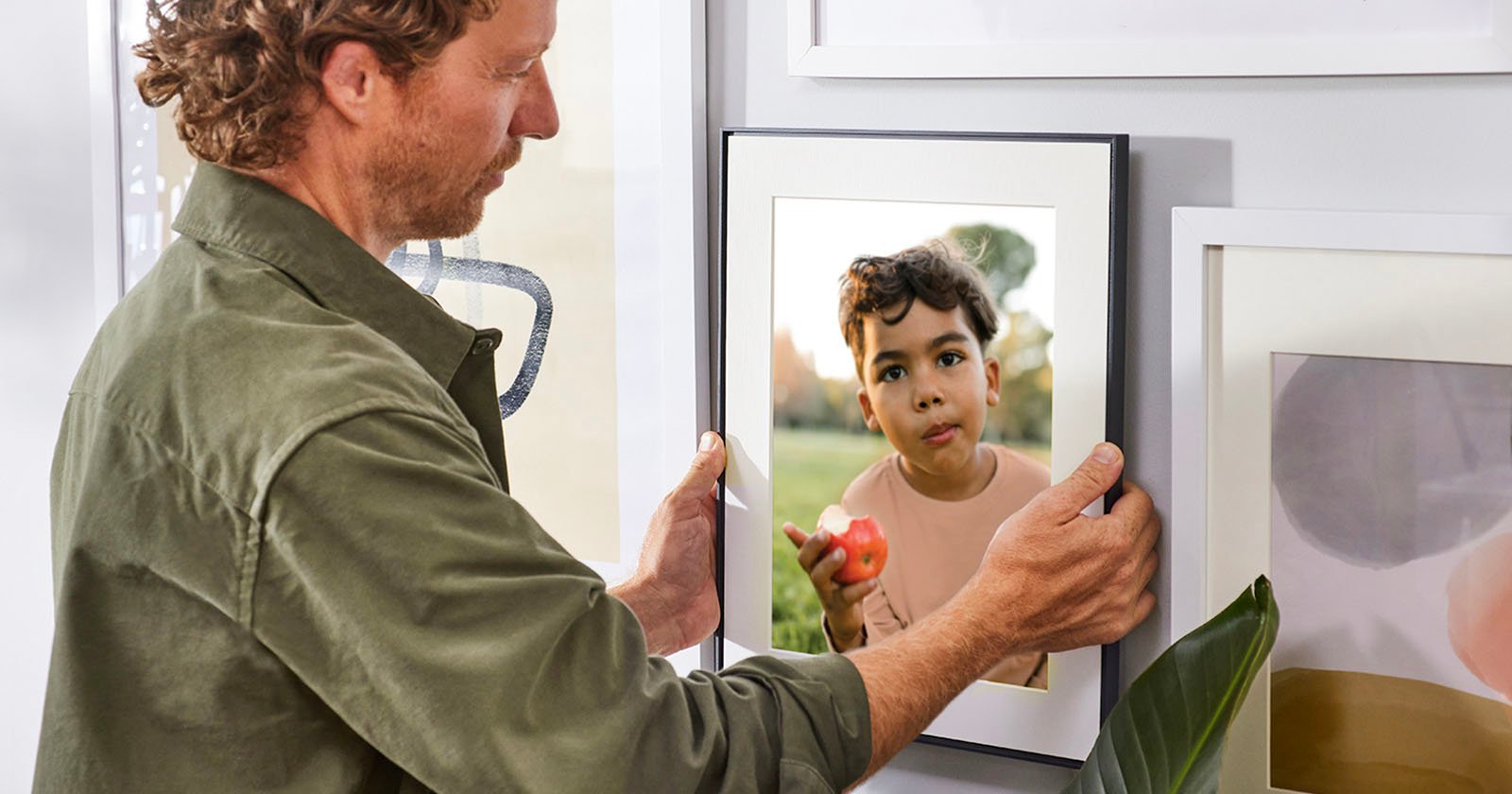 A man hangs up a photo of a child on the wall using the Aura Frames Walden model.