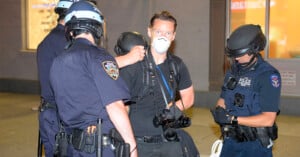 Photographer Adam Gray, wearing a mask and surrounded by officers, is arrested.