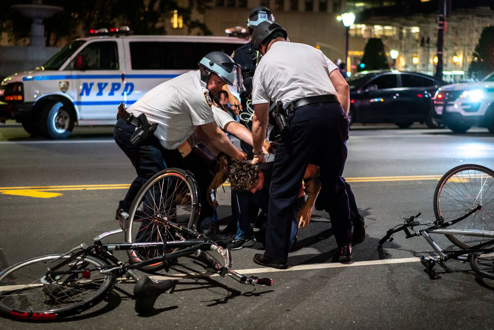 A group of police officers appear to be holding a man who is on the ground, while two bikes are seen left on the ground.