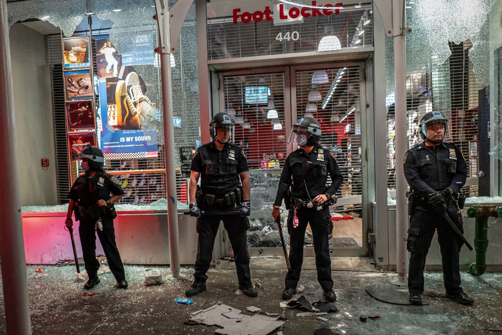 Several officers stand in front of a storefront with broken glass.