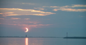 A partial eclipse is shown above a waterscape.
