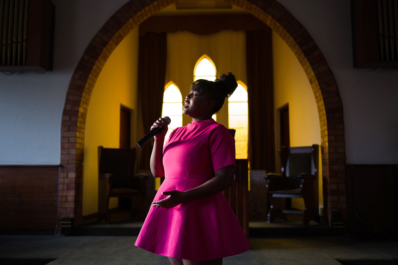 A woman in bright pink sings in a church.