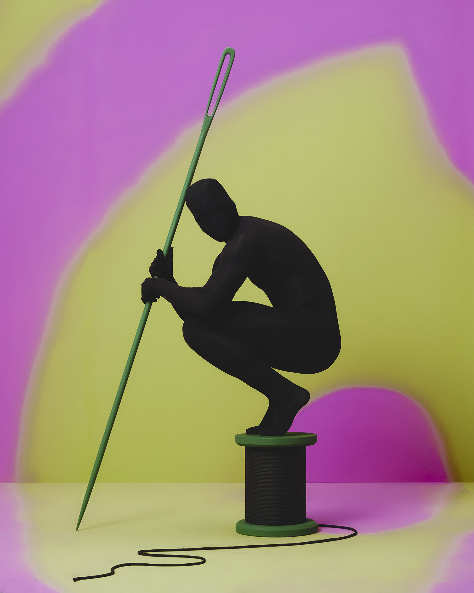 A black silhouette stands on a giant spool, holding an equally large sewing needle.