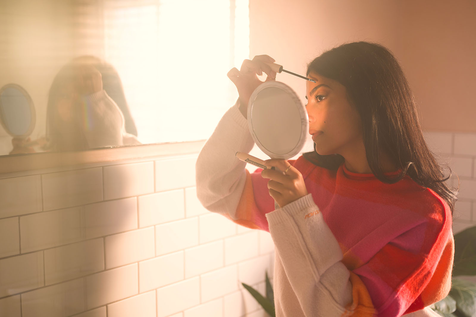 A woman fixes up her makeup with a handheld mirror in a bathroom.