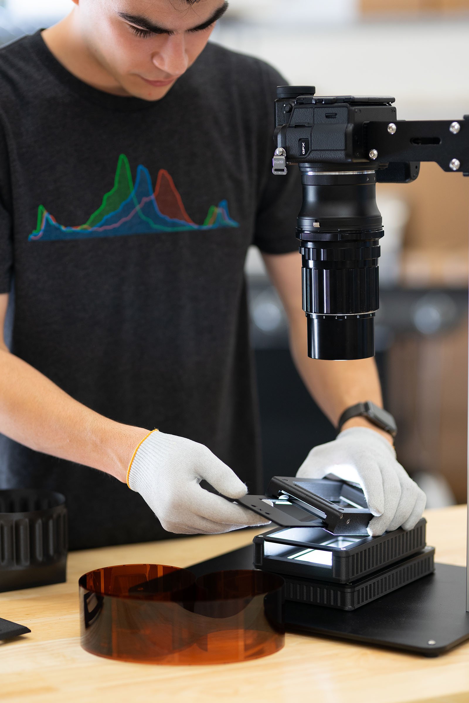 A man positions the Negative Supply Basic Film Carrier 120 MK2 while wearing gloves, and a digital camera is mounted above pointed at the tool.