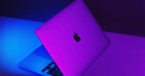 A photo shows a MacBook illuminated by purple lighting.