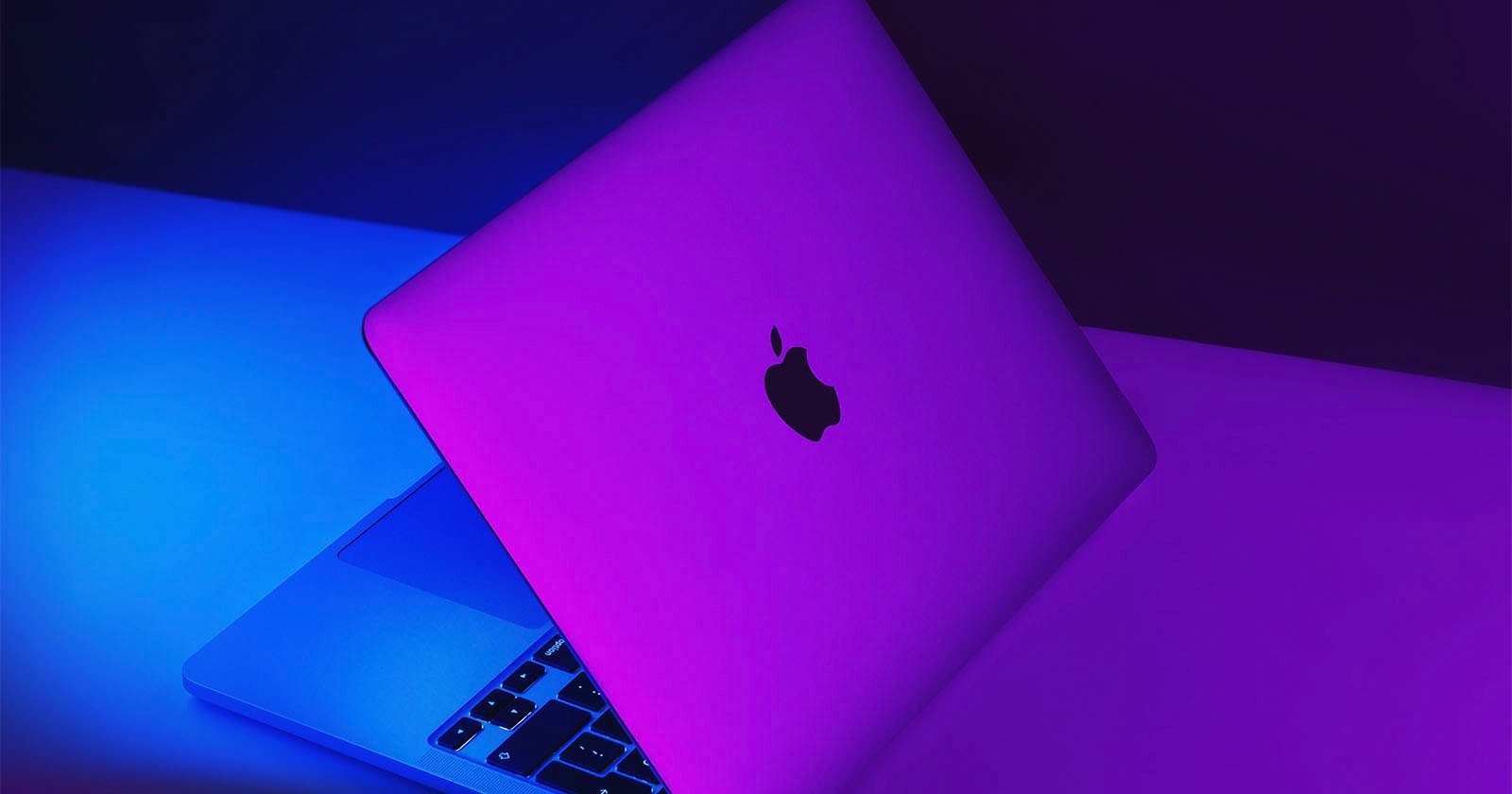 A photo shows a MacBook illuminated by purple lighting.
