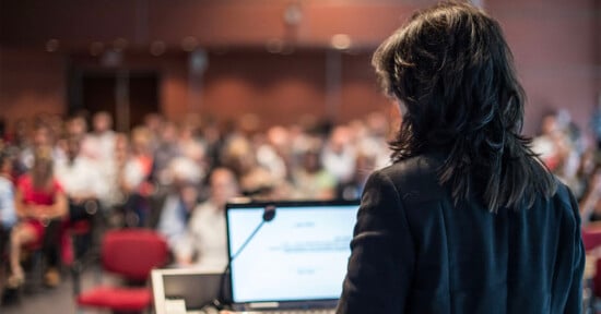 A woman speaking to a crowd is seen from behind.