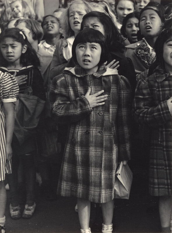 A young girl stands among other child with her hand over her hair reciting the flag pledge.