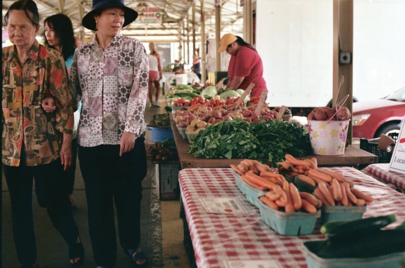 Two women walk down a row at a farmer's market.