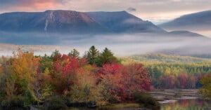 A fog rolls over fall foliage in a mountainous river valley.