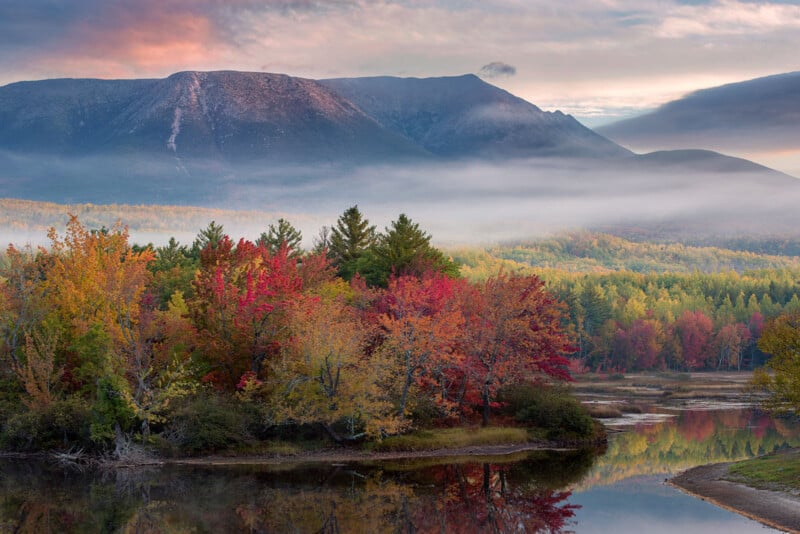 A fog rolls over fall foliage in a mountainous river valley.