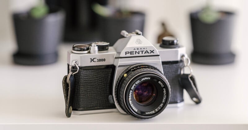 A Pentax K1000 camera sits on a shelf.