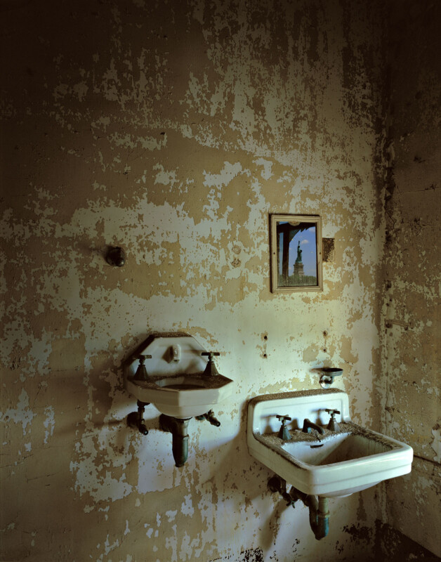 A mirror above a sink reflects the Statue of Liberty in an abandoned room.