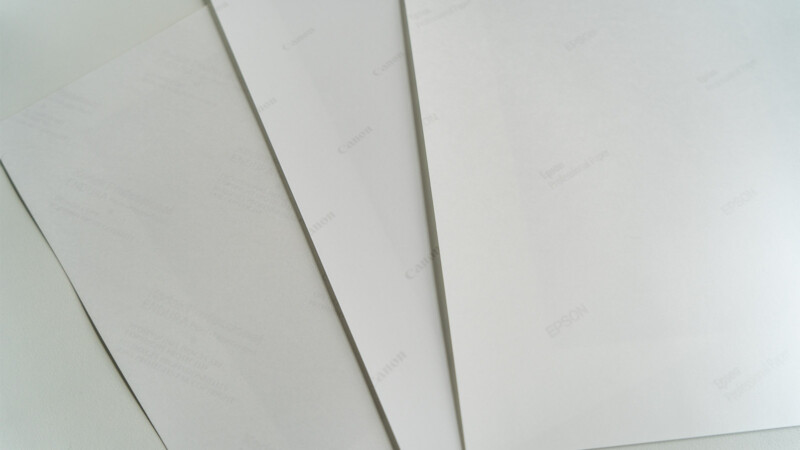 Three types of photo paper sit on a desk with the back text showing. 