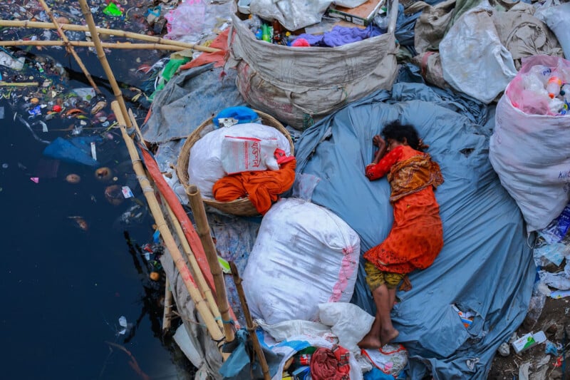 A woman sleeps among trash heaps.