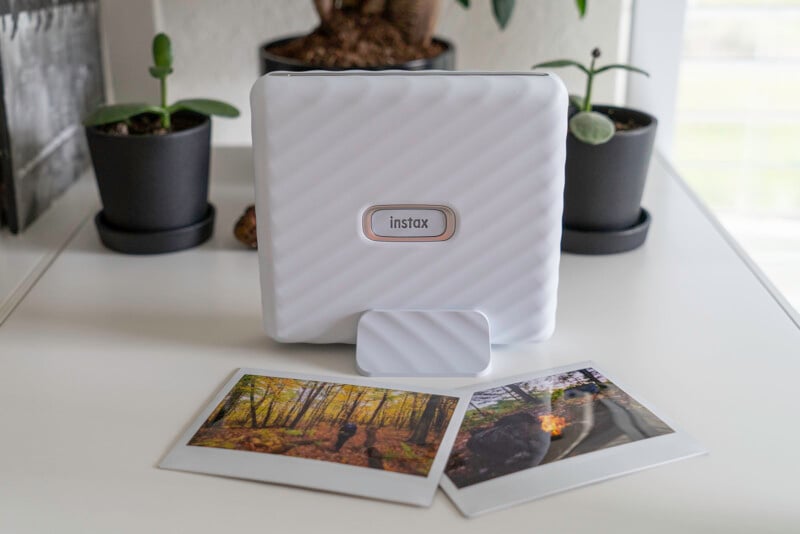 A Fujifiml Instax Link Wide photo printer sits on a shelf with two prints in front of it.