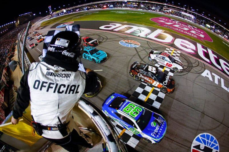 A NASCAR official in the foreground waves the checkered flag as Daniel Suárez beats Kyle Bush and Ryan Blaney across the finish line. 