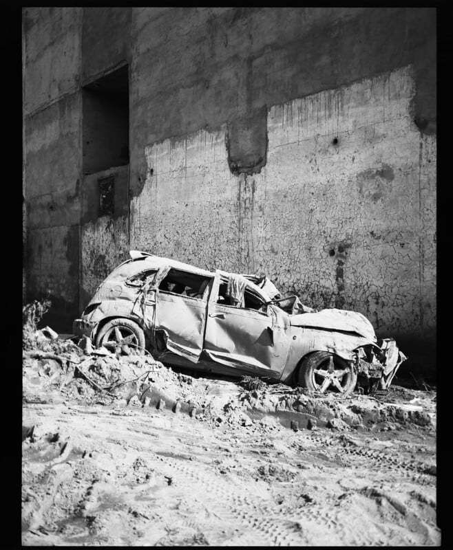 A wrecked car sits on top of rubble in a black and white image taken with Film Ferrania P33 film.