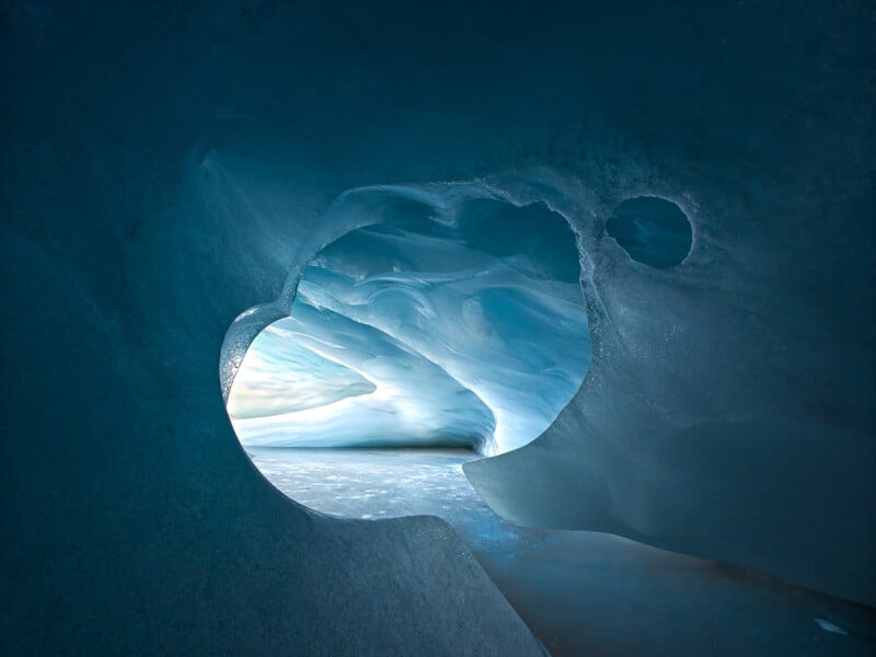 A blue ice cave has a hole that looks deeper into the cave. 