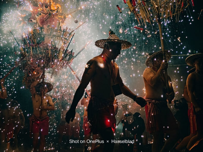 A person walks in front of fireworks and a crowd at a Fire Dragon Dancer festival at night. 