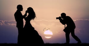 A silhouette of a wedding photographer capturing a portrait of a bride and groom at sunset.