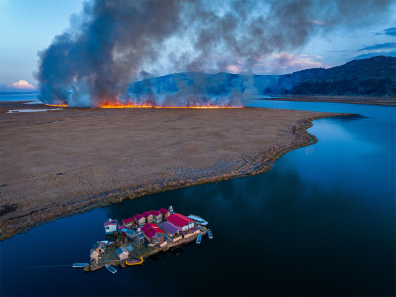 Sony World Photography Awards 2024 Open competition category winners -- travel winner. Aerial view of a coastal scene, fire on the land, boat in the water in the foreground.