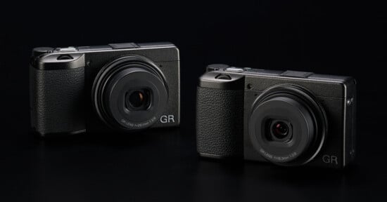 Two Ricoh GR series compact digital cameras are displayed against a black background. Both cameras have a sleek and minimalistic design, featuring prominent lenses and textured grips for easy handling. The branding "GR" is visible on the bottom right of each camera.