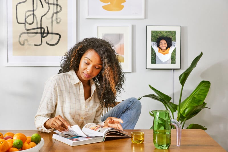 A woman sits at a table reading with the Walden Aura Frames hangs on a wall in the background.