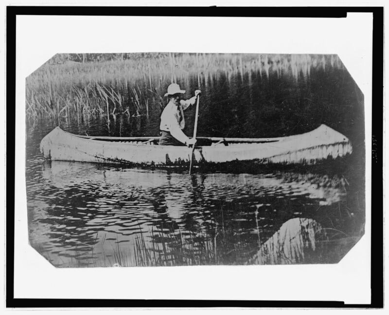 A tintype photograph captures a man paddling a canoe.