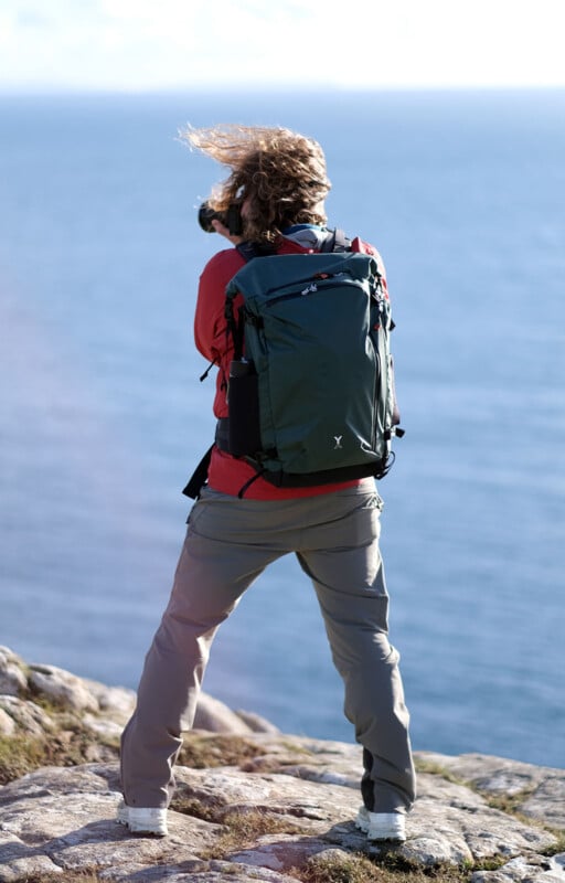 A photographer by the water takes a picture while wearing the Fjord 50-C expandable camera backpack.