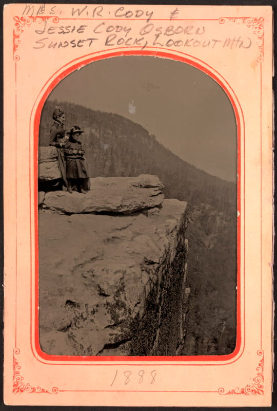 A decorative paper with orange details frames a tintype photograph of two women sitting on a cliff.