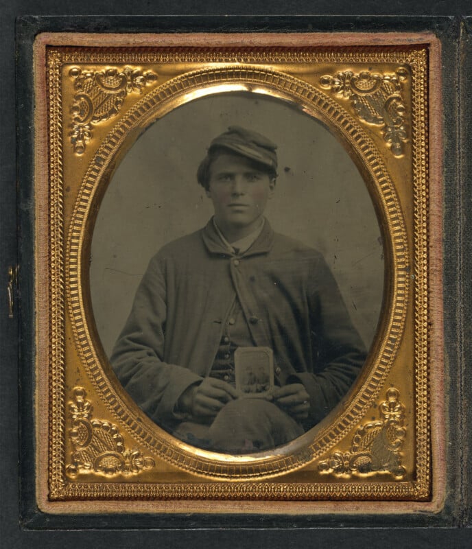 An elaborate gold frame surrounds a tintype photograph of a soldier holding a photo of his brother.