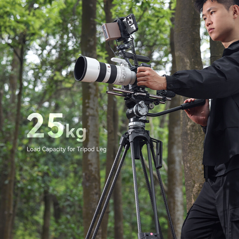 A person stands next to his camera on the Video Fast Heavy-Duty Tripod in a forest.