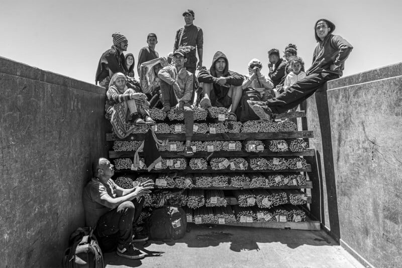 Black and white image of a group of diverse people dressed in eclectic clothing, sitting and standing around a stair-like structure filled with multiple pairs of shoes.