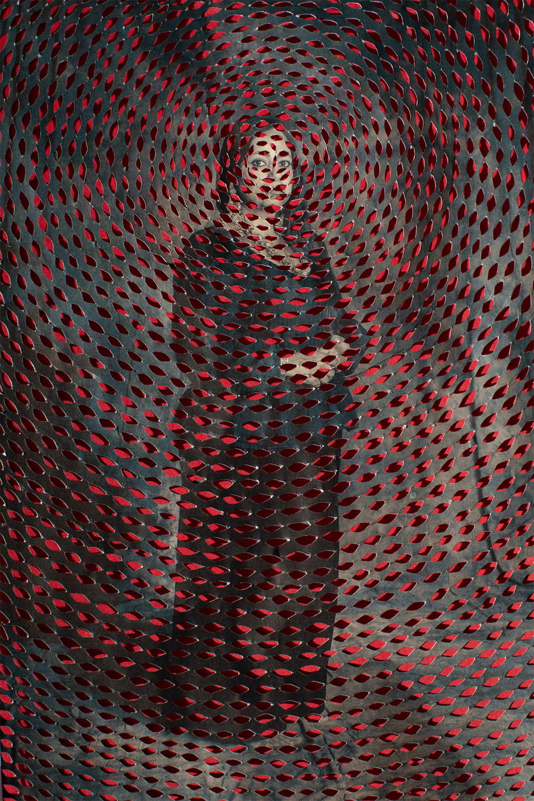 A person stands enveloped in a swirling red and black patterned texture, creating a hypnotic visual effect around their silhouette.