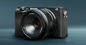A black mirrorless sony camera with an artisans lens is positioned prominently against a subdued gray background. the lens and camera labels are clearly visible.