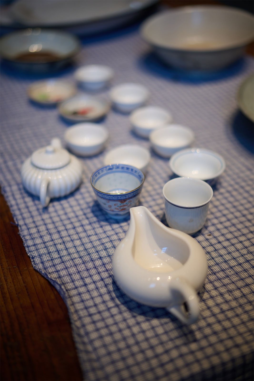 An elegant chinese tea set arranged on a blue and white checkered tablecloth, featuring a white teapot, several cups, and small dishes.
