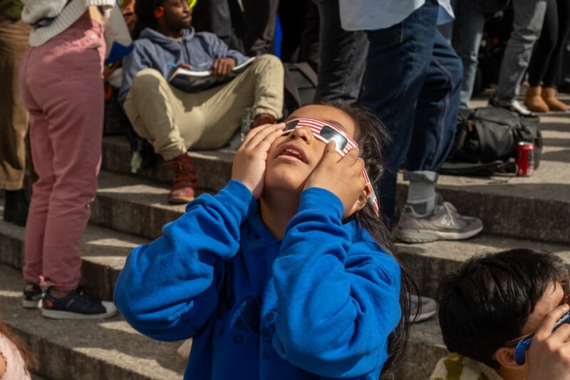A kid looks up wearing eclipse glasses.