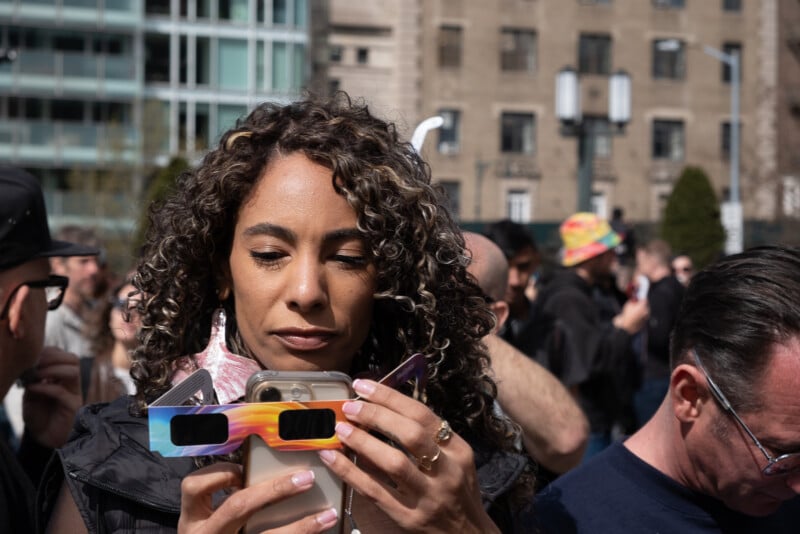 A person aims their phone at eclipse glasses.
